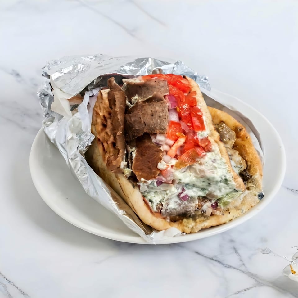 A gyro sandwich with meat, tomatoes, onions, and sauce, partially wrapped in foil on a white plate.
