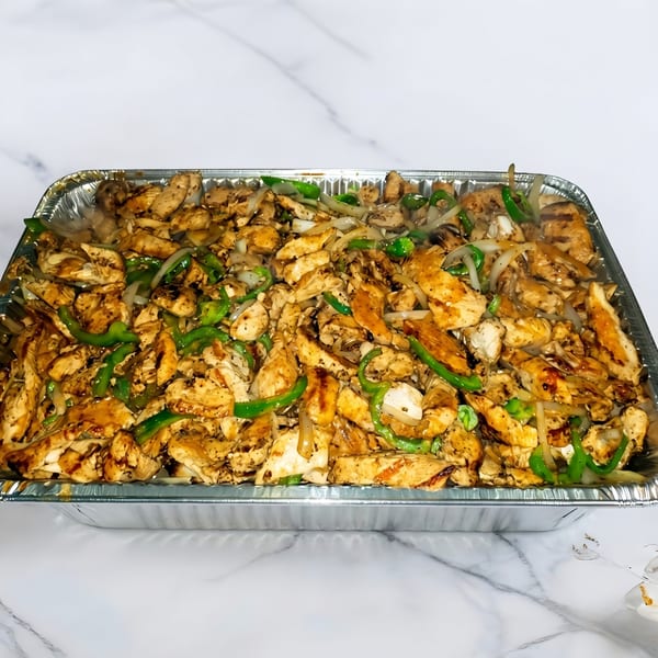 A large aluminum tray filled with sizzling chicken fajitas, green peppers, and onions.