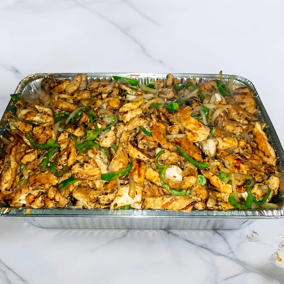 A large aluminum tray filled with sizzling chicken fajitas, green peppers, and onions.