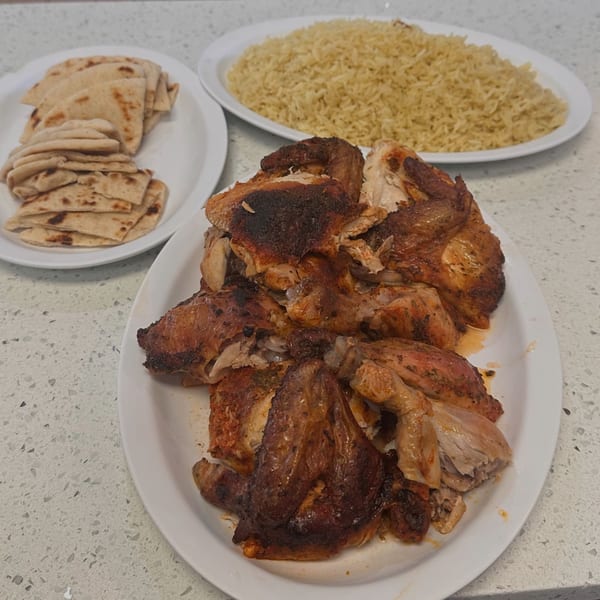 Plates of roasted chicken pieces, yellow rice, and flatbread on a white countertop.