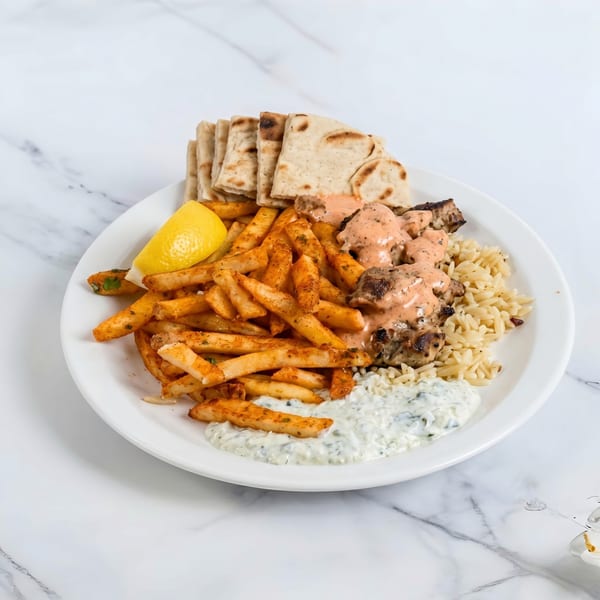 A plate of chicken souvlaki with fries, rice, pita bread, tzatziki, and a lemon wedge.